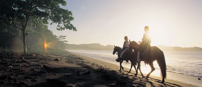 couple riding horses on beach at sunset 