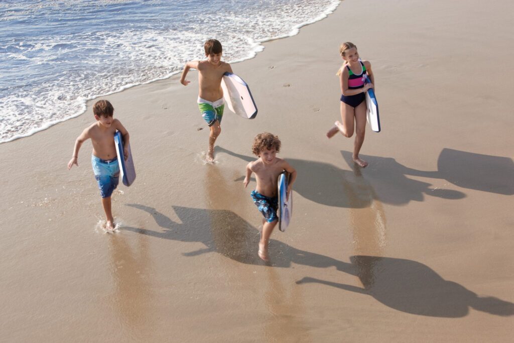 children running on the beach with boogie boards