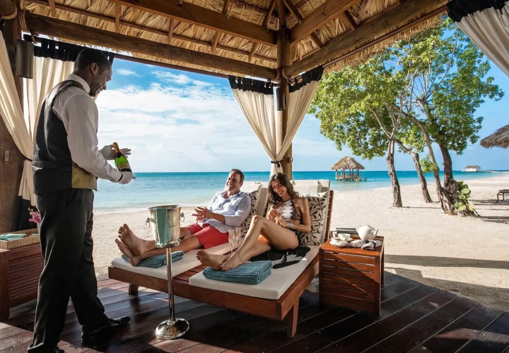 butler serving guests champagne in private beach palapa at Sandals South Coast